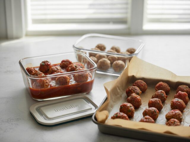 Leftover meatballs in sauce in a shallow glass container beside a tray of meatballs ready to freeze
